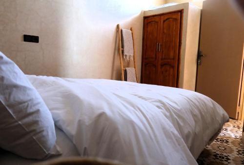 a bedroom with a white bed and a wooden door at Little Beach House Sidi Kaouki in Sidi Kaouki