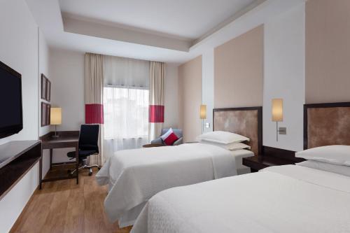a hotel room with two beds and a desk at Four Points by Sheraton Vadodara in Vadodara