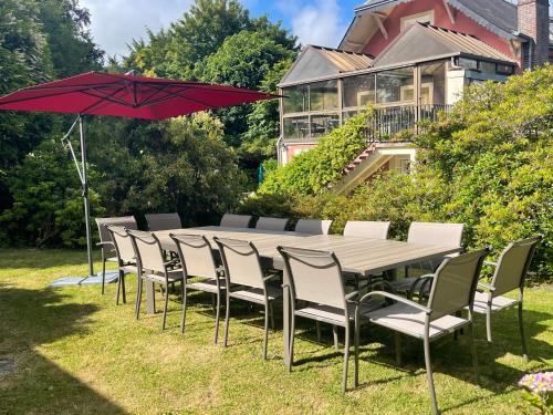 a long table and chairs with a red umbrella at Grande maison familiale aux portes d'Etretat in Criquetot-lʼEsneval