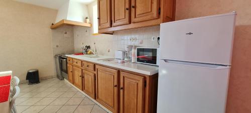 La cuisine est équipée d'un réfrigérateur blanc et de placards en bois. dans l'établissement Gite le petit village 7 kms du Zoo de Beauval, à Saint-Romain-sur-Cher