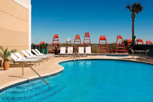 a swimming pool with chairs and red chairs at Four Points by Sheraton Jacksonville Beachfront in Jacksonville Beach