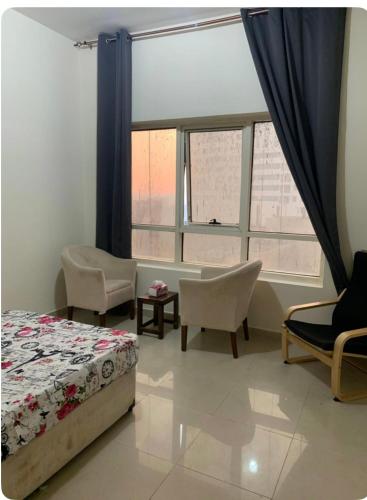 a bedroom with a bed and chairs and windows at SHJ DXB Sunny Border Guesthouse in Dubai