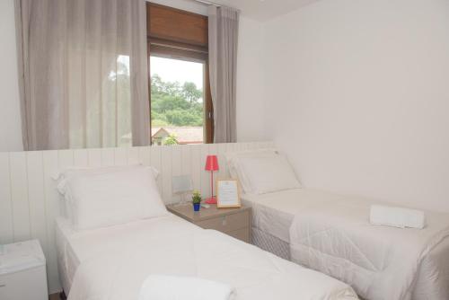 a white bedroom with two beds and a window at Haute Haus - Guest House in Florianópolis