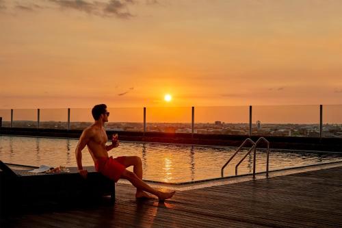 a man sitting on the edge of a pool with the sunset at Four Points by Sheraton Makassar in Makassar