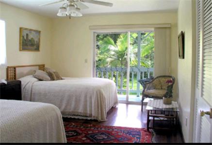 Lava Tree Tropic Inn في Pahoa: غرفة نوم بسريرين وباب زجاجي منزلق