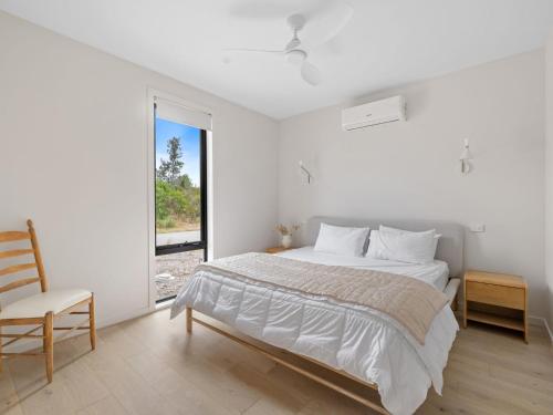 a white bedroom with a bed and a chair at Wirilda Retreat in Inverloch