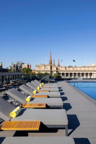a row of chaise lounges next to a pool at Le Meridien Melbourne in Melbourne