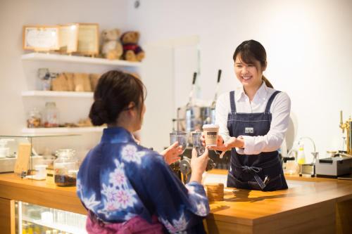 a woman is handing a cup to a woman in a kitchen at TSUCHIYA Kinosaki onsen in Toyooka