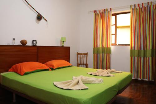a bedroom with a bed with green sheets and orange pillows at O Jardim do Vinho, AC in Praia