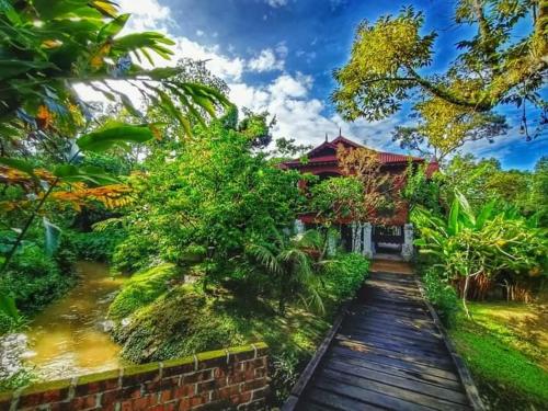a wooden walkway leading to a house with a pond at Bagas Zakariah Orchard Lodge in Gopeng
