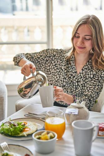 Eine Frau, die an einem Tisch mit einer Tasse Kaffee sitzt. in der Unterkunft Paris Marriott Opera Ambassador Hotel in Paris