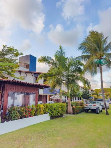a building with palm trees in front of a yard at Casa com jacuzzi piscina e comodidade a beira mar in Maragogi