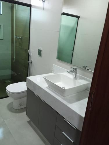 a bathroom with a sink and a toilet and a mirror at Casa Alto Padrão Parque Leste - Compartilhada in Lavras