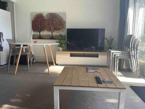 a living room with a flat screen tv and a table at Comfortable townhouse with aircon, huge balcony & hot tub in Auckland