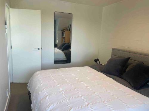 a bedroom with a white bed and a mirror at Luxury townhouse with aircon, huge balcony & hot tub in Auckland