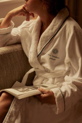 a woman sitting on a couch reading a book at The Tasman, a Luxury Collection Hotel, Hobart in Hobart