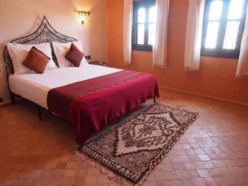 a bedroom with a bed with a red blanket and a rug at Riad Bouchedor in Ouarzazate