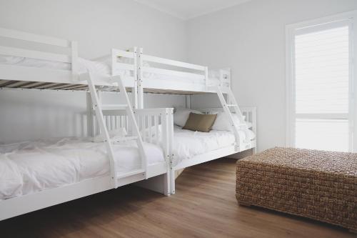 a bedroom with two white bunk beds and a ottoman at The Arv in Robe