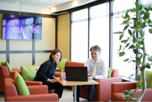 a man and woman sitting at a table with a laptop at Hotel ARU KSP in Kawasaki