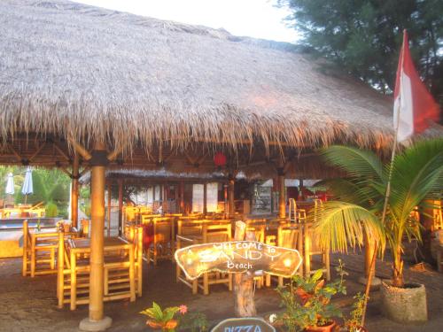 a restaurant with a straw hut with tables and chairs at Sandy Beach Bungalows in Gili Islands