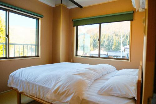 a bed in a room with two windows at Schanze Nozawa in Nozawa Onsen