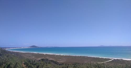 a view of a beach with blue water and trees at Seascape Peninsula Bach in Kaitaia