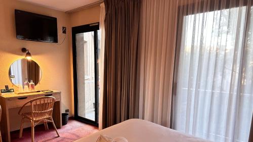 a hotel room with a bed and a desk and a window at Logis hotel Noemys Gradignan in Gradignan