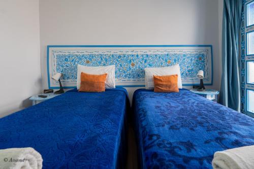 two beds in a room with blue sheets and orange pillows at Casa Familia in Chefchaouene