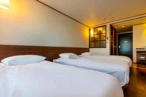 three beds in a room with white sheets at Tamara Jeju hotel in Seogwipo
