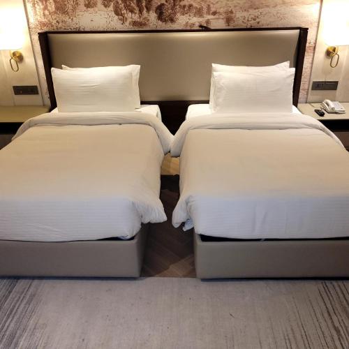 two beds in a hotel room with white sheets and pillows at The Tivoli New Delhi in New Delhi