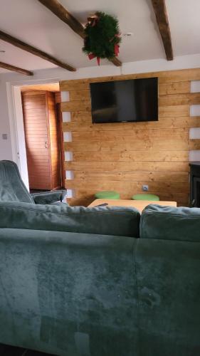 a living room with a green couch and a flat screen tv at Gîtes Les Grandes Voies - Clé Vacances in Le Ménil
