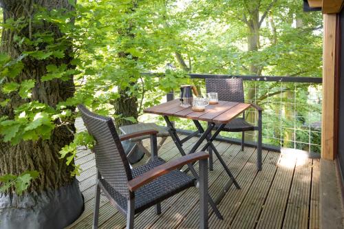 a wooden table and chairs on a deck with trees at Baumhaus Beletage in Bockhop