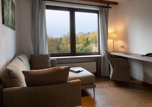 a living room with a couch and a desk and a window at Hotel Land Gut Höhne in Mettmann