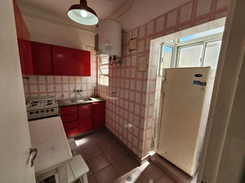 a small kitchen with red cabinets and a refrigerator at 2 ambientes frente a plaza Colón y playas del centro in Mar del Plata