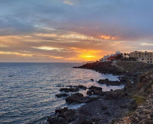 a sunset over the ocean with buildings on a rocky shore at Los Abrigos 2 apartments Guest House Ocean relax, wifi, playas in Los Abrigos