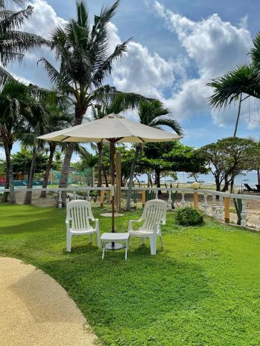 two white chairs and an umbrella on the grass at Gold View Beachfront Resort in Timbaon
