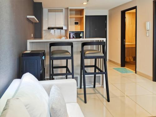 a kitchen with two bar stools in a living room at Newly 1BR Apt Cikarang with Pool, Gym & Wi-Fi by 2ndHome in Leuweungmalang