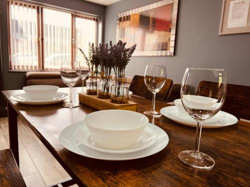 a wooden table with plates and wine glasses on it at MODERN SUITES -5 Bedroom House- With FREE PARKING Birmingham city in Birmingham