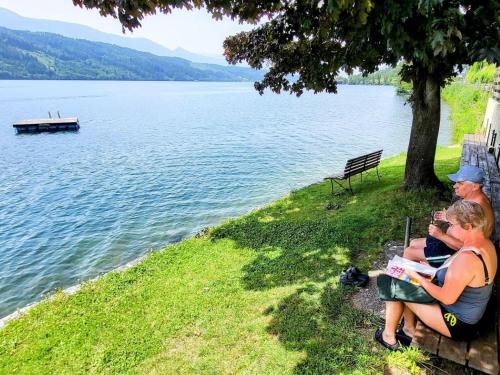 two people sitting on a bench next to a lake at Pension Sedlak in Millstatt