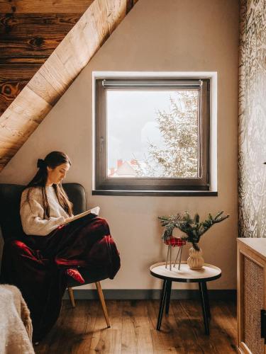 a woman sitting in a chair reading a book in a window at Okno w Gorce-magiczny apartament na uboczu nad jeziorem Czorsztyńskim, Velo Czorsztyn, Szczawnica, Zakopane in Maniowy
