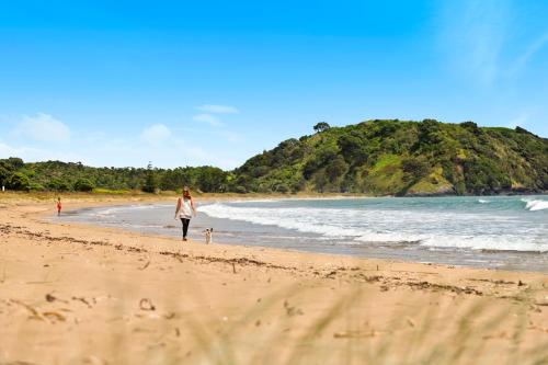 a woman walking a dog on the beach at Taipa Beach Resort in Taipa