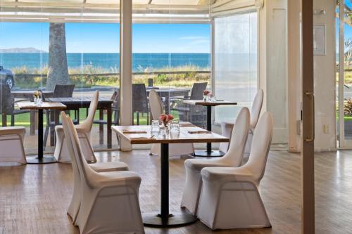 a restaurant with white chairs and tables and windows at Taipa Beach Resort in Taipa