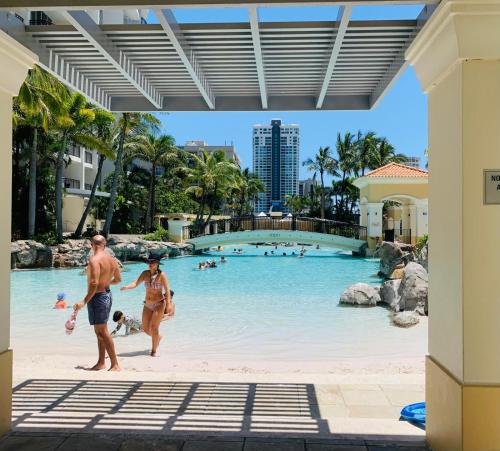 a man and woman walking through a pool at a resort at Bellagio@Chevron, Luxe, 2 Bedroom Apartment in the Heart of Surfers Paradise! in Gold Coast