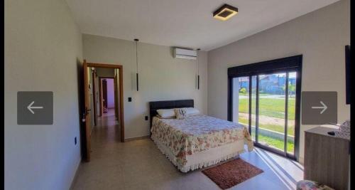 ein Schlafzimmer mit einem Bett und einem großen Fenster in der Unterkunft Casa Completa Condomínio Rosa Internacional - ao lado Sufland - Garopaba-SC in Garopaba