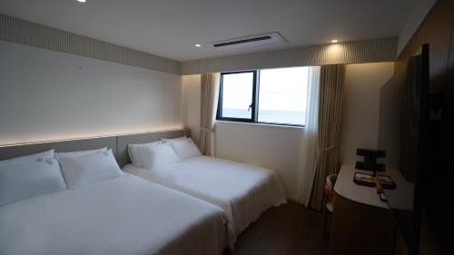 a hotel room with two beds and a window at H avenue Songjeong in Busan