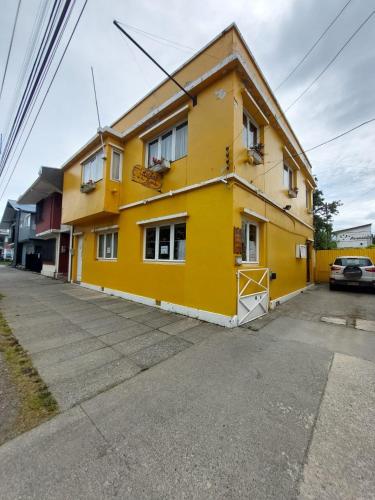 a yellow house on a street with a parking lot at Hostal de la Avenida in Punta Arenas