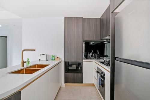 a kitchen with white cabinets and a stainless steel refrigerator at Stylish 2BR Apt with Pool & Views Near Parramatta in Sydney