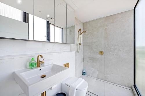 a white bathroom with a sink and a shower at Stylish 2BR Apt with Pool & Views Near Parramatta in Sydney