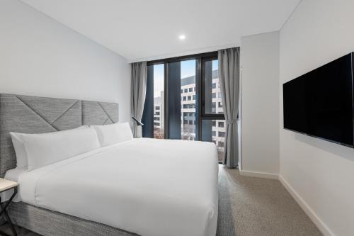 a white bedroom with a large bed and a flat screen tv at Meriton Suites Canberra in Canberra