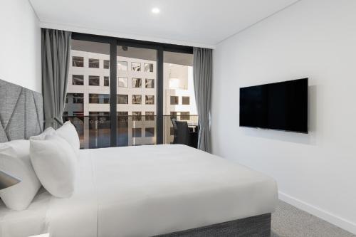 a bedroom with a white bed and a flat screen tv at Meriton Suites Canberra in Canberra